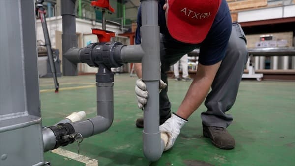 An employee wearing an ATX company hat is connecting pipes.